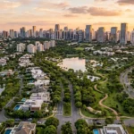 Vista aérea de Alphaville ao entardecer, mostrando condomínios residenciais de alto padrão, áreas verdes, lagos e o skyline de prédios modernos ao fundo.