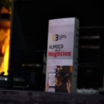 Totem do 63° Almoço de Negócios do C3 – O Clube da Construção Civil sobre balcão escuro, destacando a identidade visual do evento em ambiente sofisticado.
