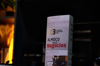 Totem do 63° Almoço de Negócios do C3 – O Clube da Construção Civil sobre balcão escuro, destacando a identidade visual do evento em ambiente sofisticado.