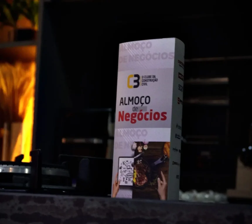 Totem do 63° Almoço de Negócios do C3 – O Clube da Construção Civil sobre balcão escuro, destacando a identidade visual do evento em ambiente sofisticado.