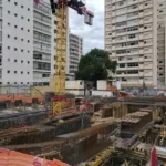 Canteiro de obras com montagem de vigas estruturais pré-armadas em área urbana, destacando a atuação da Aços Urano em projeto de alta complexidade.