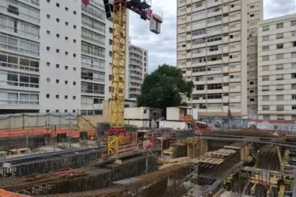 Canteiro de obras com montagem de vigas estruturais pré-armadas em área urbana, destacando a atuação da Aços Urano em projeto de alta complexidade.