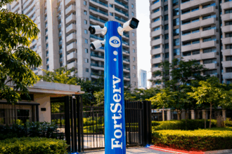 Totem de segurança FortServ com câmeras de vigilância instaladas na entrada de um condomínio residencial moderno, cercado por prédios altos e áreas verdes.