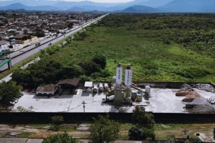 Vista aérea da filial Guarujá da Concreserv, mostrando a unidade de concreto usinado ao lado de uma rodovia movimentada e áreas verdes, com a cidade e montanhas ao fundo.