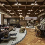 Ambiente sofisticado com sala de estar, jantar e biblioteca integrados, mobiliário sob medida SCA, tons amadeirados e forro treliçado, projeto de Denise Barretto para a Mostra Artefacto 2026.