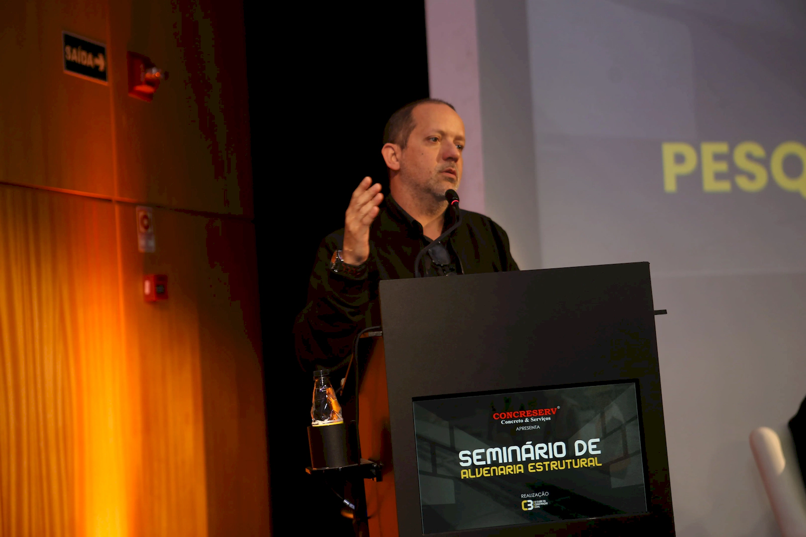 Rodolfo Zagallo, CEO do C3 - O Clube da Construção Civil, discursa no palco durante o Seminário de Alvenaria Estrutural, ao lado de um púlpito com a identidade visual do evento.