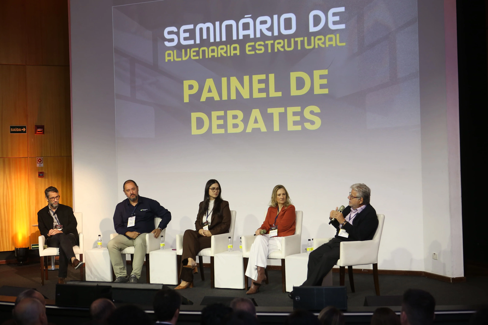 Painel de especialistas debate tendências e desafios da alvenaria estrutural durante o Seminário de Alvenaria Estrutural do C3, com cinco profissionais sentados no palco do auditório.