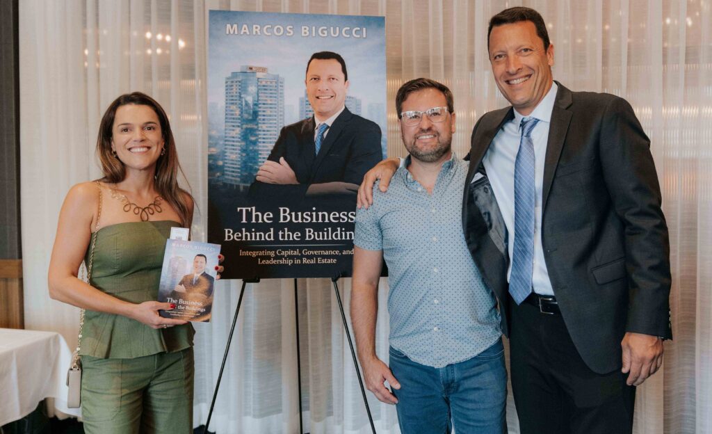Ana e Fábio Moraes posam sorridentes ao lado do autor Marcos Bigucci durante o lançamento do livro “The Business Behind the Buildings” em Orlando, Flórida, em junho de 2026.