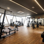 Academia moderna e sofisticada com equipamentos de musculação, esteiras e halteres, piso de madeira e iluminação em LED, projetada para empreendimentos residenciais de alto padrão.