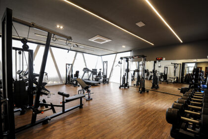 Academia moderna e sofisticada com equipamentos de musculação, esteiras e halteres, piso de madeira e iluminação em LED, projetada para empreendimentos residenciais de alto padrão.