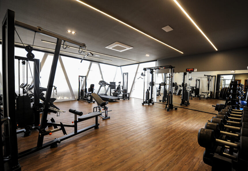 Academia moderna e sofisticada com equipamentos de musculação, esteiras e halteres, piso de madeira e iluminação em LED, projetada para empreendimentos residenciais de alto padrão.