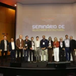 Grupo de palestrantes e painelistas do Seminário de Alvenaria Estrutural do C3 - O Clube da Construção Civil, posando juntos no palco do auditório, com o telão ao fundo exibindo o nome do evento.