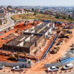 Obras de saneamento da Concrejato em andamento na Grande São Paulo, com trabalhadores instalando tubulações de água e máquinas pesadas em um canteiro cercado por bairros residenciais.
