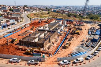 Obras de saneamento da Concrejato em andamento na Grande São Paulo, com trabalhadores instalando tubulações de água e máquinas pesadas em um canteiro cercado por bairros residenciais.