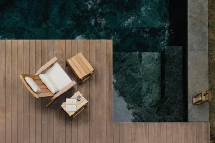 Poltrona deck da linha Marco da Tidelli, inspirada na cadeira Adirondack, com puff e mesa lateral em madeira, posicionados sobre deck ao lado de piscina.