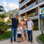 Família brasileira de classe média recebe as chaves do novo apartamento financiado pela Faixa 4 do Minha Casa Minha Vida, sorrindo em frente ao prédio moderno.