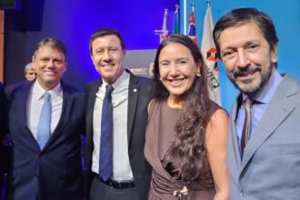 Quatro líderes do setor público e privado posam sorrindo durante a cerimônia de posse da diretoria do Secovi-SP, com bandeiras ao fundo e iluminação azul.