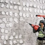 Operador utiliza martelete demolidor Hilti TE 600-AVR com exoesqueleto EXO-T-22 em obra, removendo revestimento de parede de concreto com segurança e ergonomia.