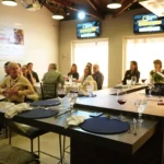 Profissionais da construção civil participam de momento de integração e networking durante o 66° Almoço de Negócios do C3, em ambiente moderno, com mesas redondas e apresentação ao vivo.