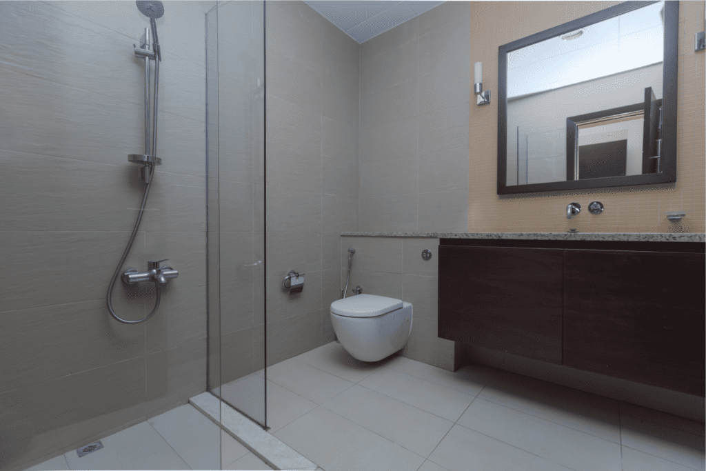 Imagem de um banheiro residencial, com chuveiro, box, vaso sanitário e armário embaixo da pia. 