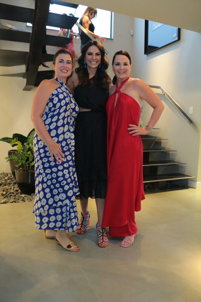 Três mulheres elegantes utilizando vestidos longos de festa olhando para a foto sorrindo.
